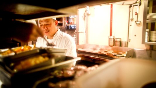 chef cooking on open flat-top grill at food court open kitchen