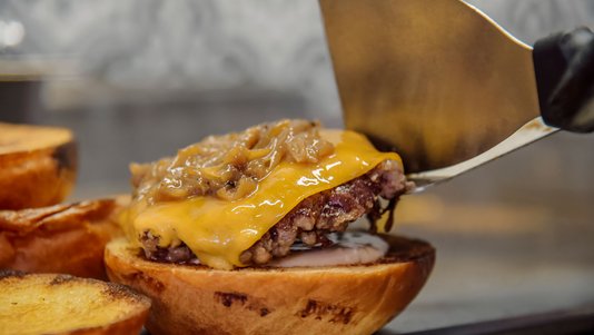 chef placing cooked burger patty onto bun at QSR assembly line