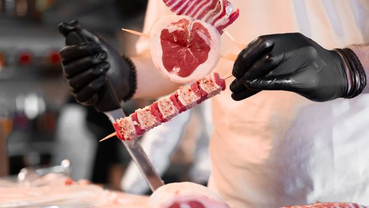 butcher with gloves preparing raw meat portions on a block