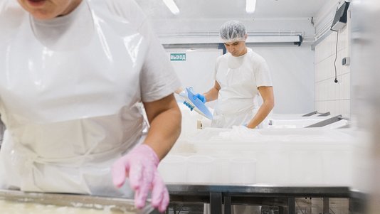 food factory workers in white coats coating food on a production line