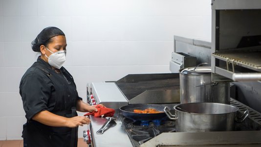 chef in face mask working at central prep kitchen station