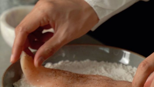 cook coating chicken fillet in flour at a breading station