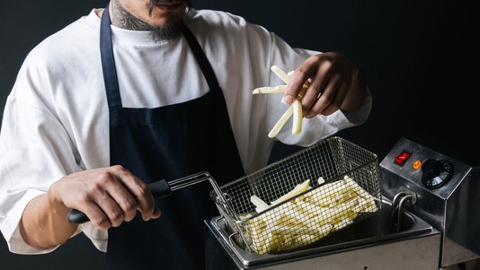 fries in a commercial deep fryer basket at a burger kitchen fry line