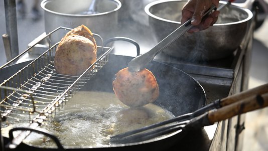 street food vendor frying snacks in oil at a small stall